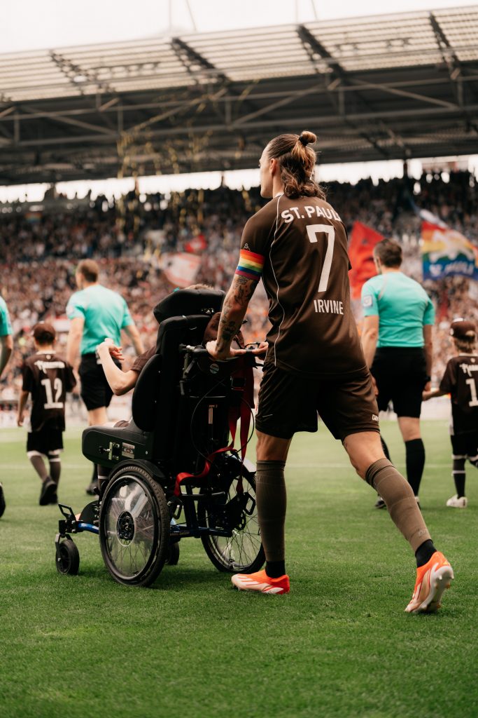 St. Pauli football captain Jackson Irvine assisiting a person on a wheelchair.