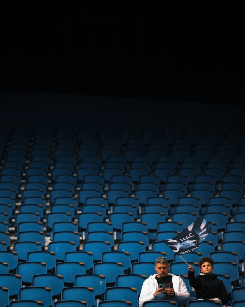 A father and son, sitting in a football stadium. The boy is waving a flag.
