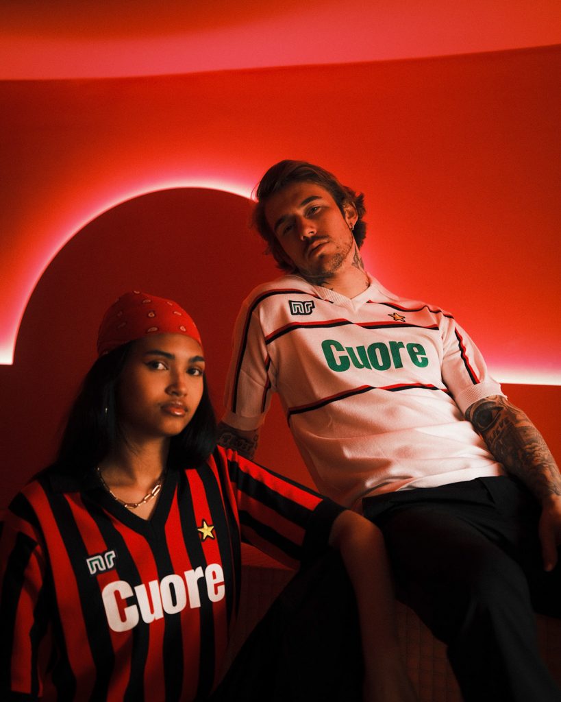 A man and a woman are sitting down together. Both are wearing vintage football jerseys 