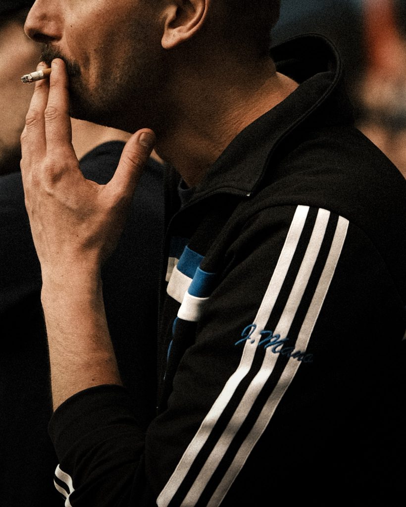 A man wearing a vintage football jersey and smoking a cigarette.