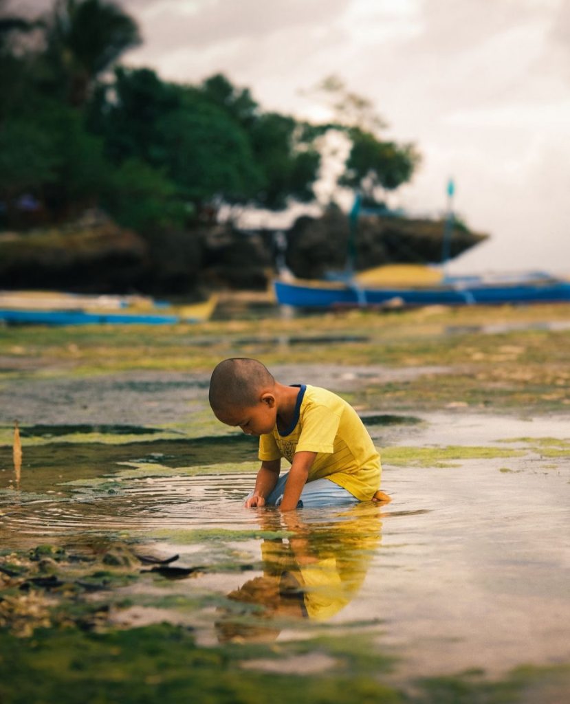 A young boy, sitting down in a puddle in the Phillipines.
